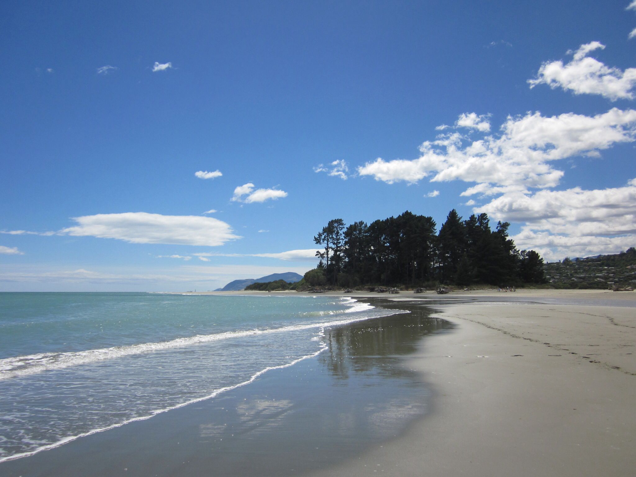 Beautiful sunny beach in Nelson, New Zealand, with golden sand, clear blue waters, and a bright sky.